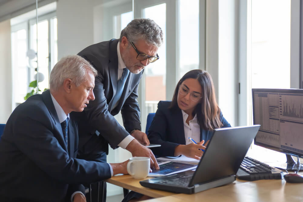 concentrated-colleagues-watching-statistic-charts-talking-about-work-professional-senior-managers-young-assistant-preparing-business-plan-teamwork-management-partnership-concept (1)