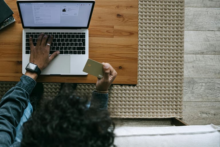 Um homem sentado em uma mesa, segurando um cartão na mão e um notebook aberto à sua frente, enquanto realiza um pagamento online.