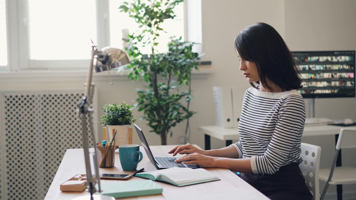 Mulher sentada em frente a um computador, em uma mesa de escritório, trabalhando. 