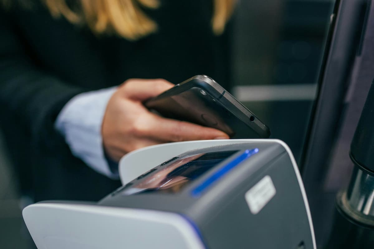 A mão de um homem segurando um celular enquanto faz um pagamento digital.