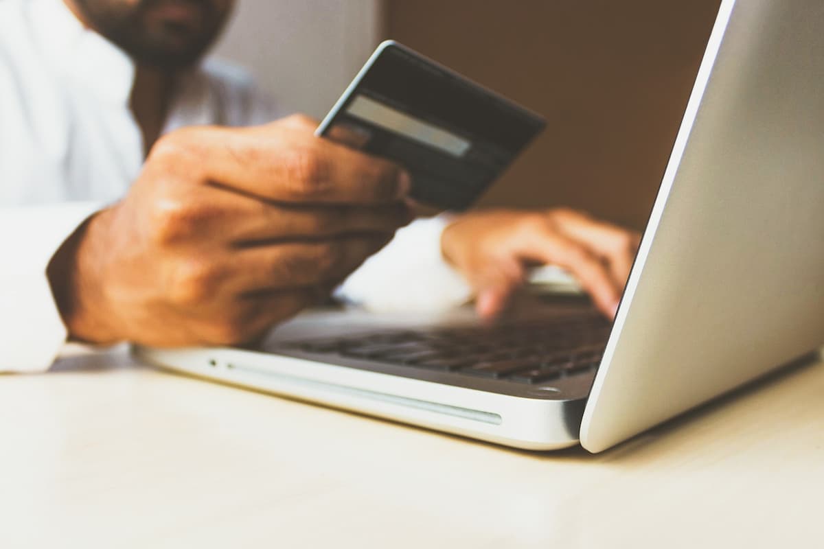 Homem sentado em uma mesa fazendo pagamento online com cartão de crédito no notebook. 